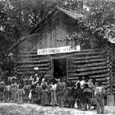 Members of the Freedmen's Colony stand in front of a log structure on Roanoke Island