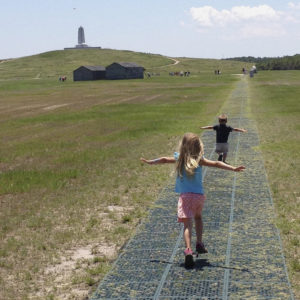 Two children, a girl and a boy, with their arms outstretched run along the path of the first flight at Wright Brothers National Memorial.