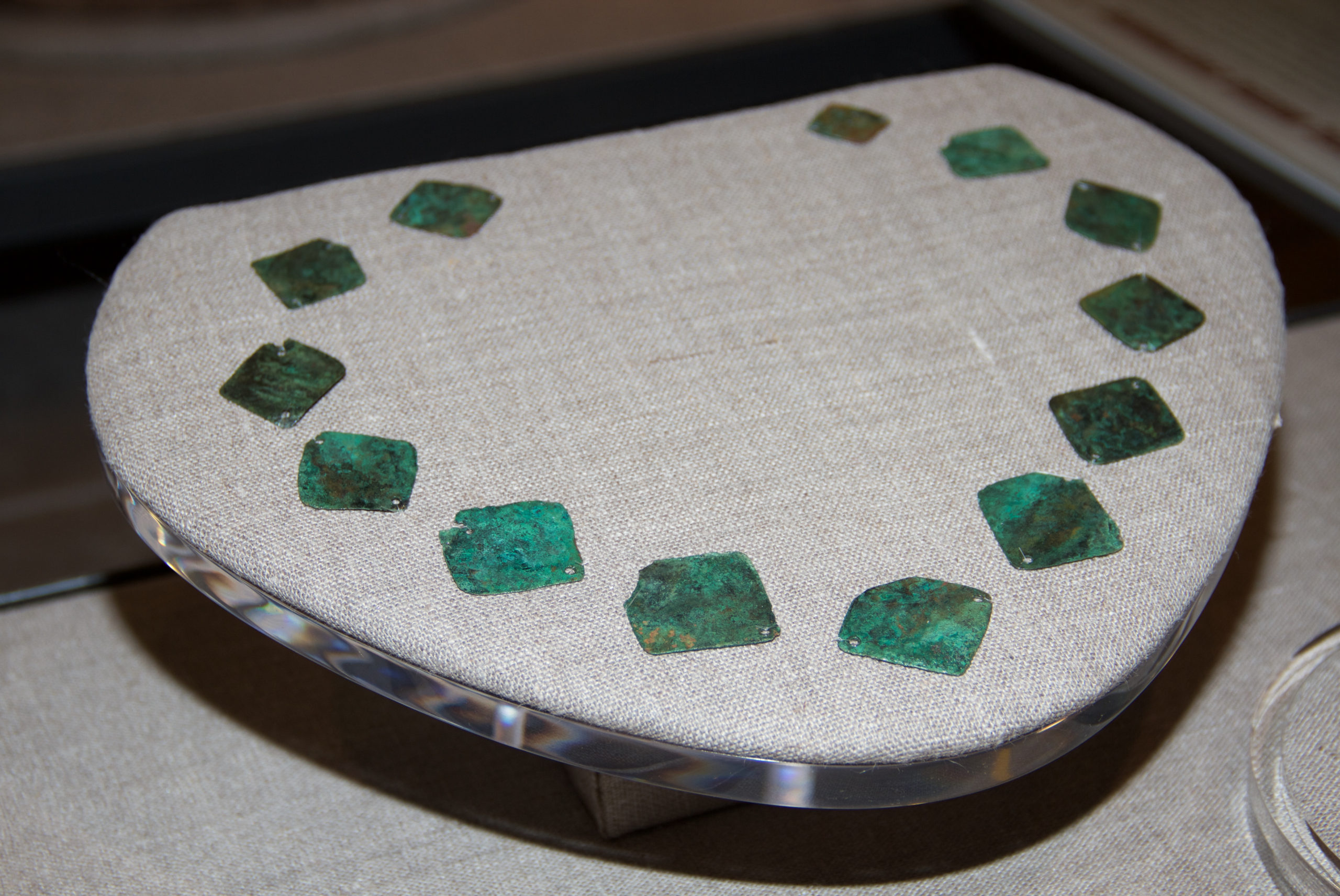 This necklace was likely the elaborate personal ornament of a Roanoke Indian. The necklace consists of 13 diamond-shaped plates made of copper from continental Europe that were strung together on short, knotted cords, which have now rotted away.