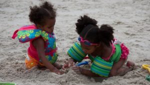 Two little girls play in the sand while wearing life jackets. 