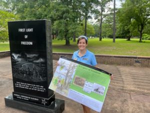 Latino Heritage Internship Program Intern Isabel Gonzalez holds the educational wayside sign she created about the Freedmen's Colony while standing next to the First Light of Freedom Monument at Fort Raleigh National Historic Site. 