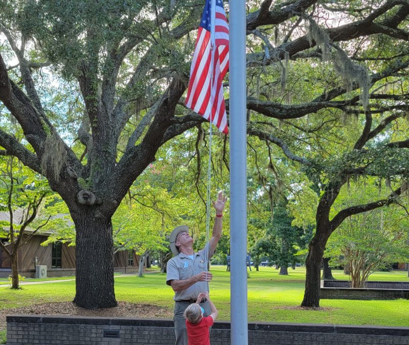 A young visitor helps Volunteer Paul Hinds lower the American flag at Fort Raleigh National Historic Site.