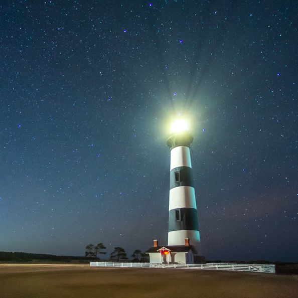 The Bodie Island Lighthouse, with black and white horizontal bands, shines at night.