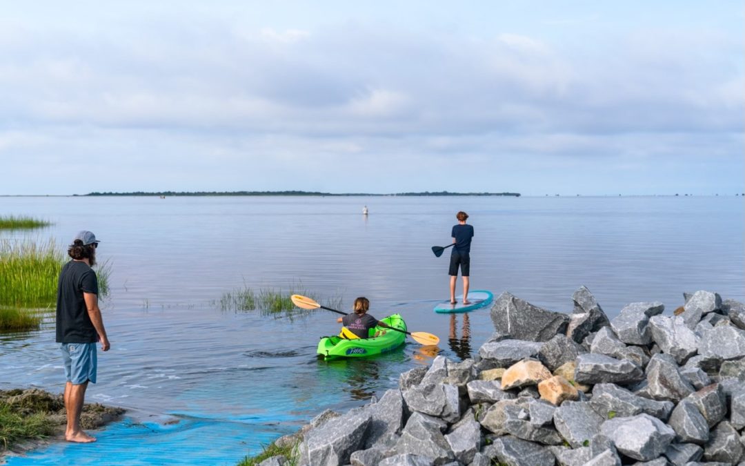 A family enjoying the new Oregon Inlet Kayak Launch. One youth is standing on a paddleboard and one youth is in a kayak while an adult looks on.