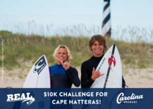 Two young surfers stop for a picture on the beach of Cape Hatteras National Seashore. The Cape Hatteras Lighthouse is in the background.