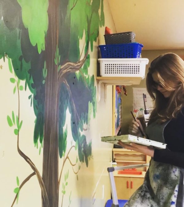 Artist Karyn Renea Soto painting a mural featuring a tree.