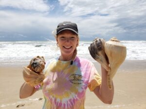 Ranger Alisa holding four large whelk shells she found while beachcombing on Cape Hatteras National Seashore in her free time.