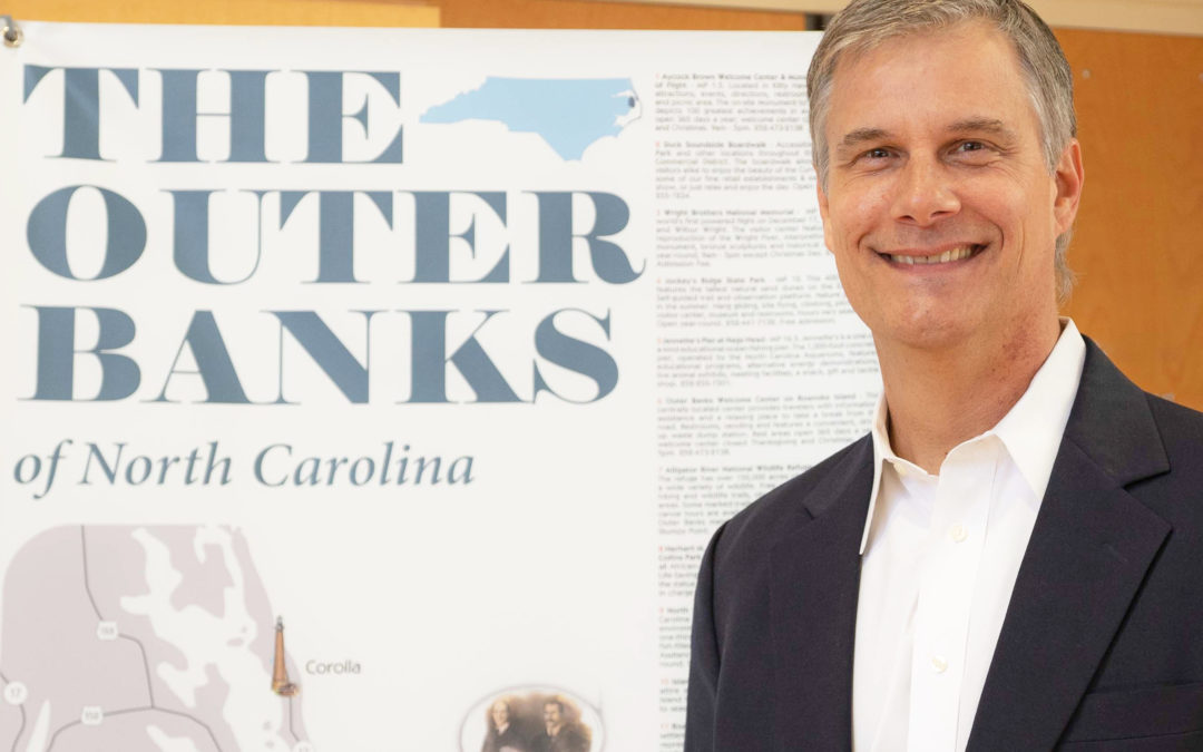 Lee Nettles, Executive Director of the Outer Banks Visitors Bureau, in front of a map of the Outer Banks of North Carolina.
