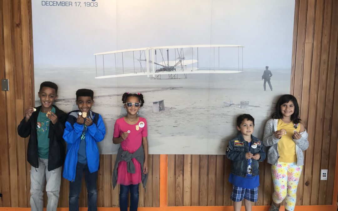 Five Junior Rangers (three on left, two on right) stand in front of the first flight photograph at Wright Brothers National Memorial.