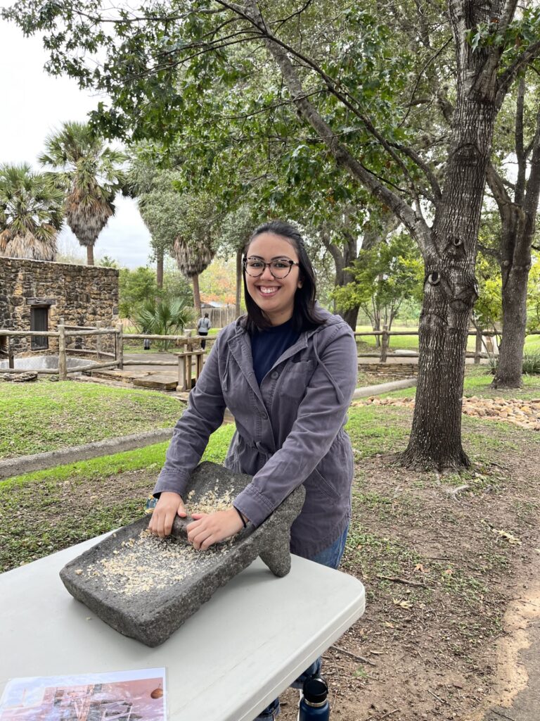 Community Volunteer Ambassador Serena Diaz using a mano and metate.